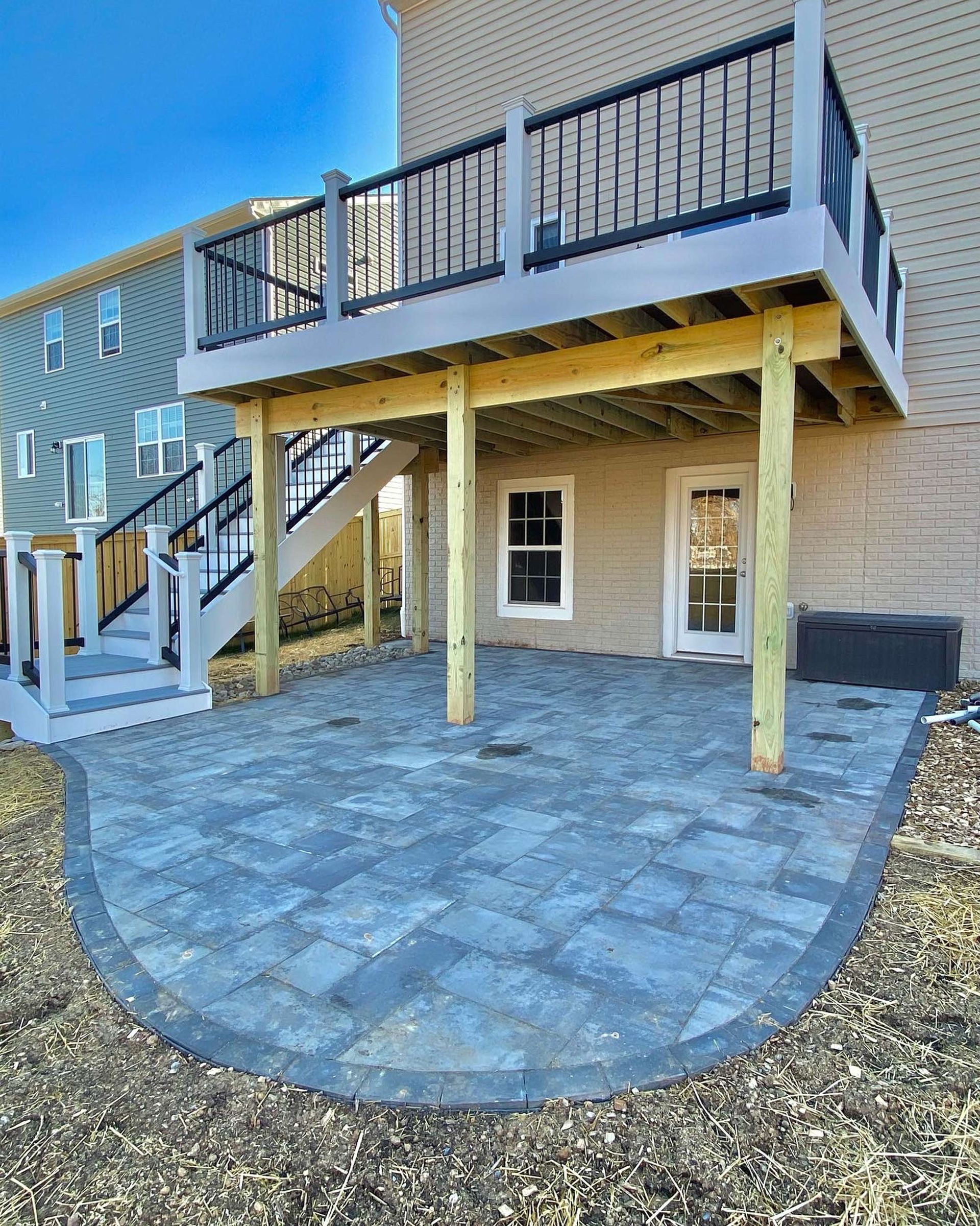 A large deck with stairs and a patio in front of a house.