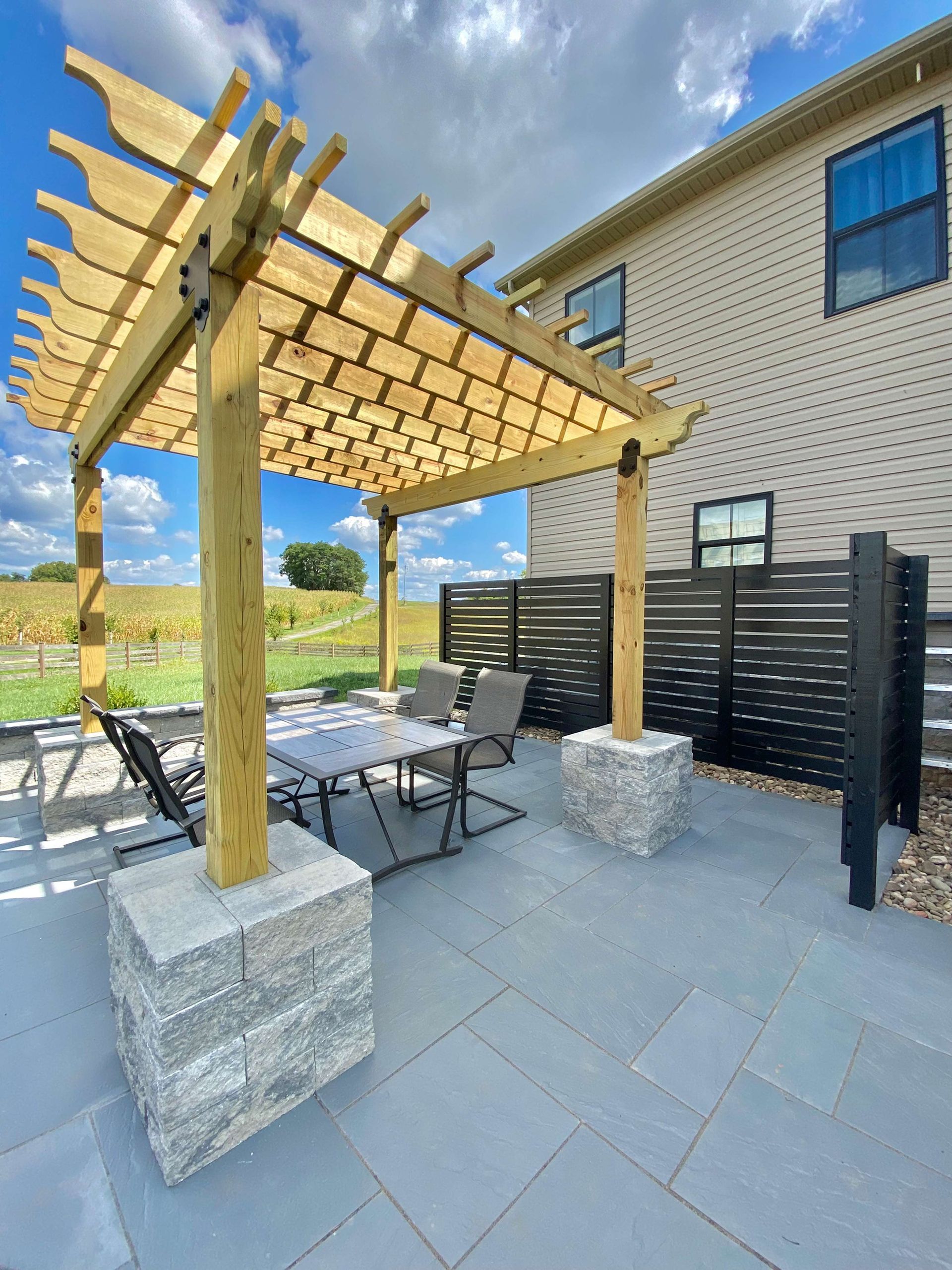 A wooden pergola is sitting on top of a patio next to a house.