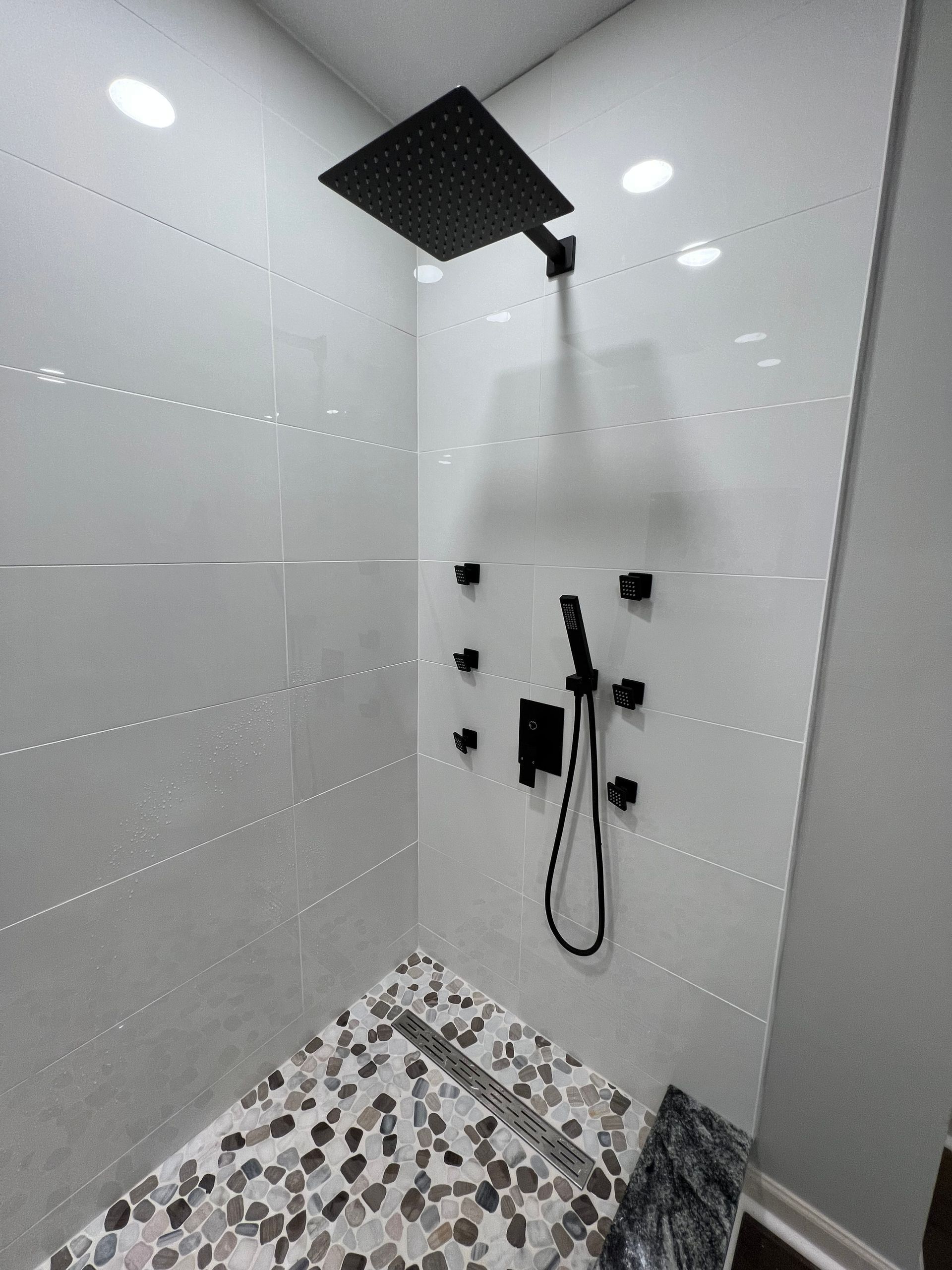A shower with a black shower head and a tiled floor.