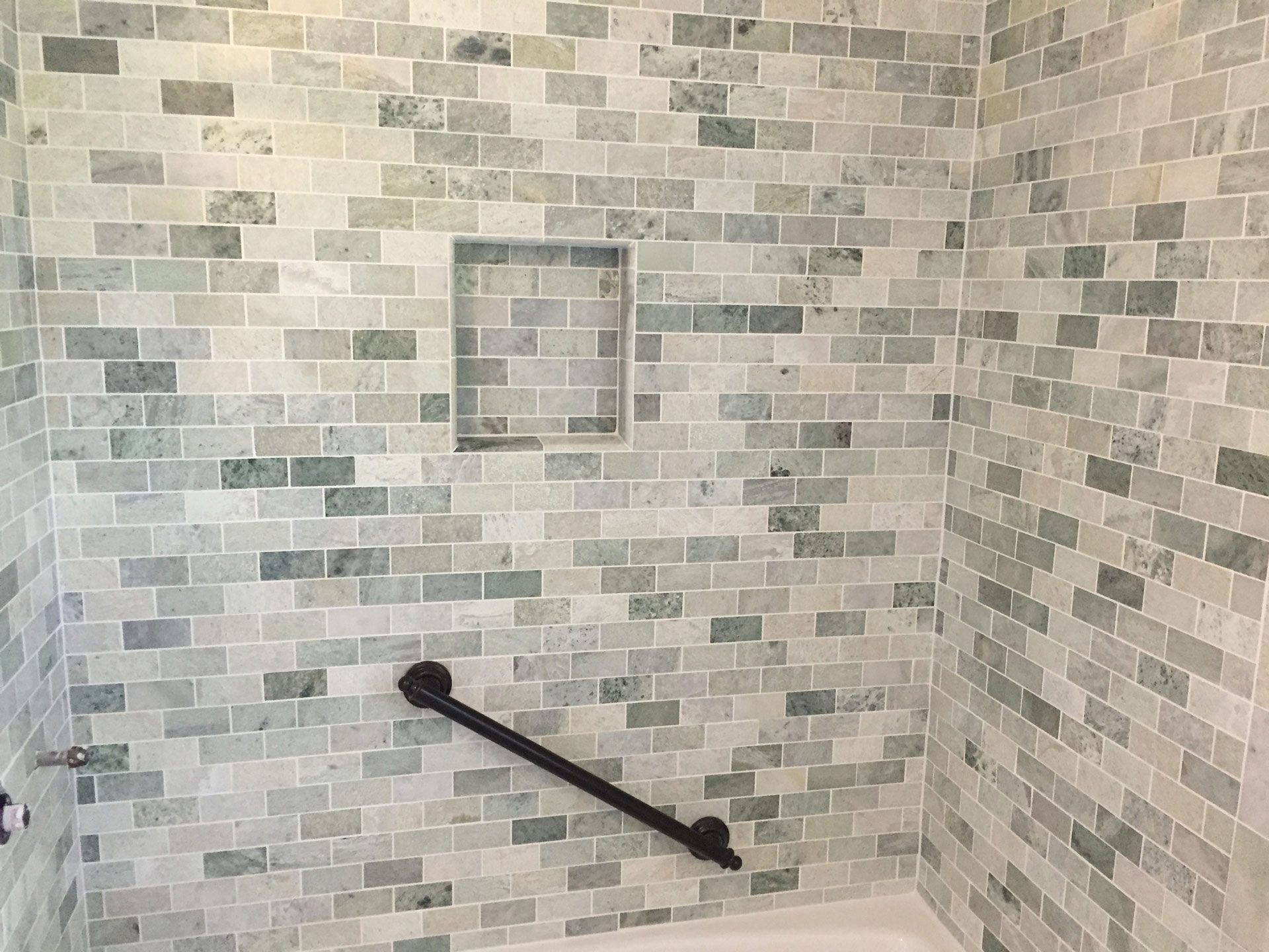 A bathroom shower with a brick wall and a black handle.
