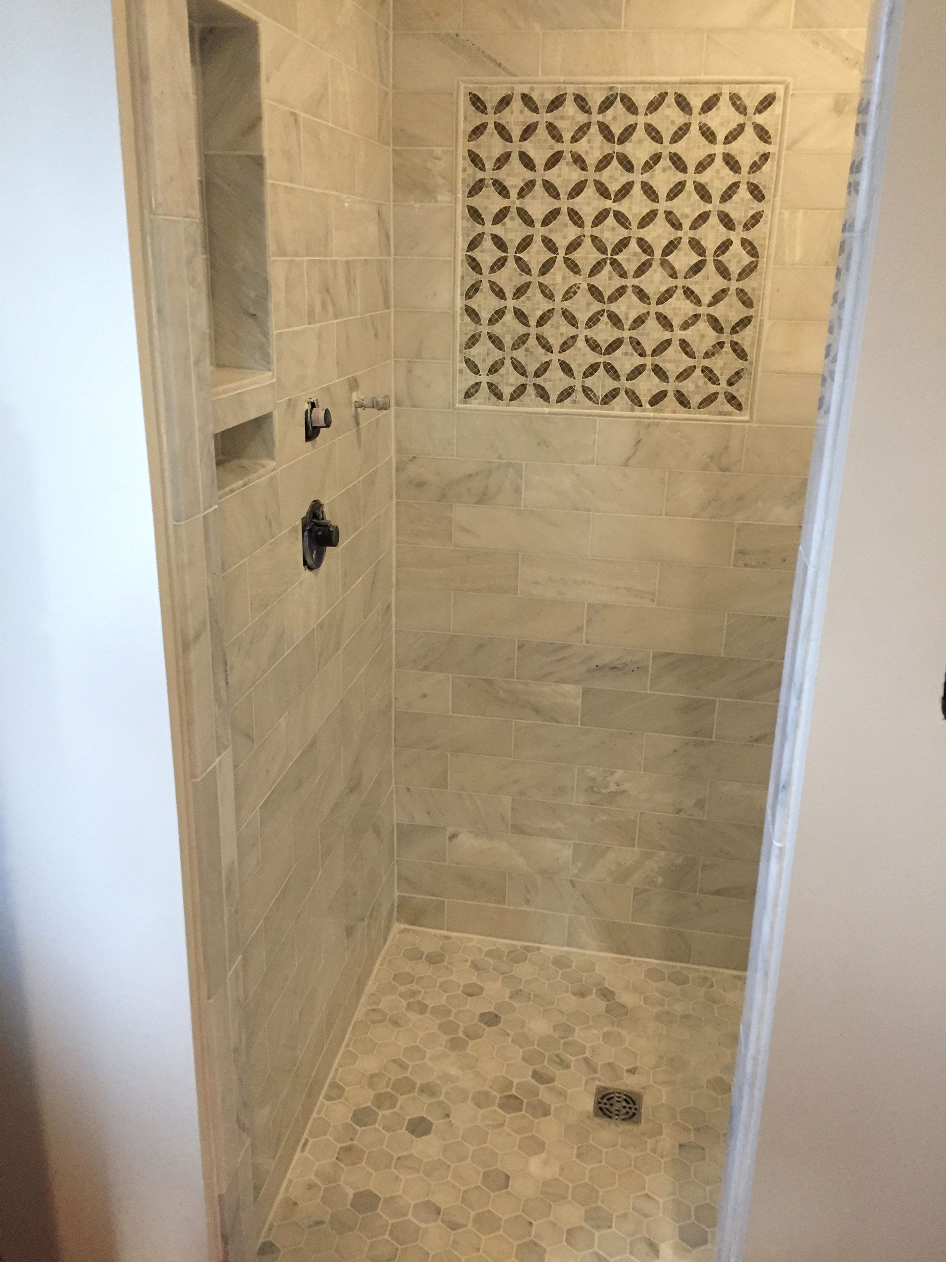 A walk in shower with a geometric pattern on the wall.