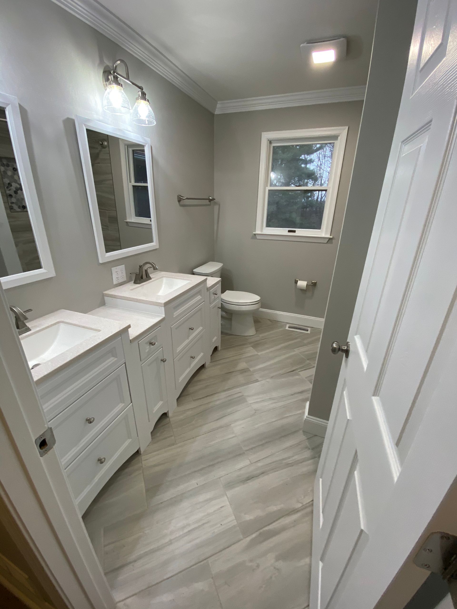 A bathroom with two sinks , a toilet , and two mirrors.