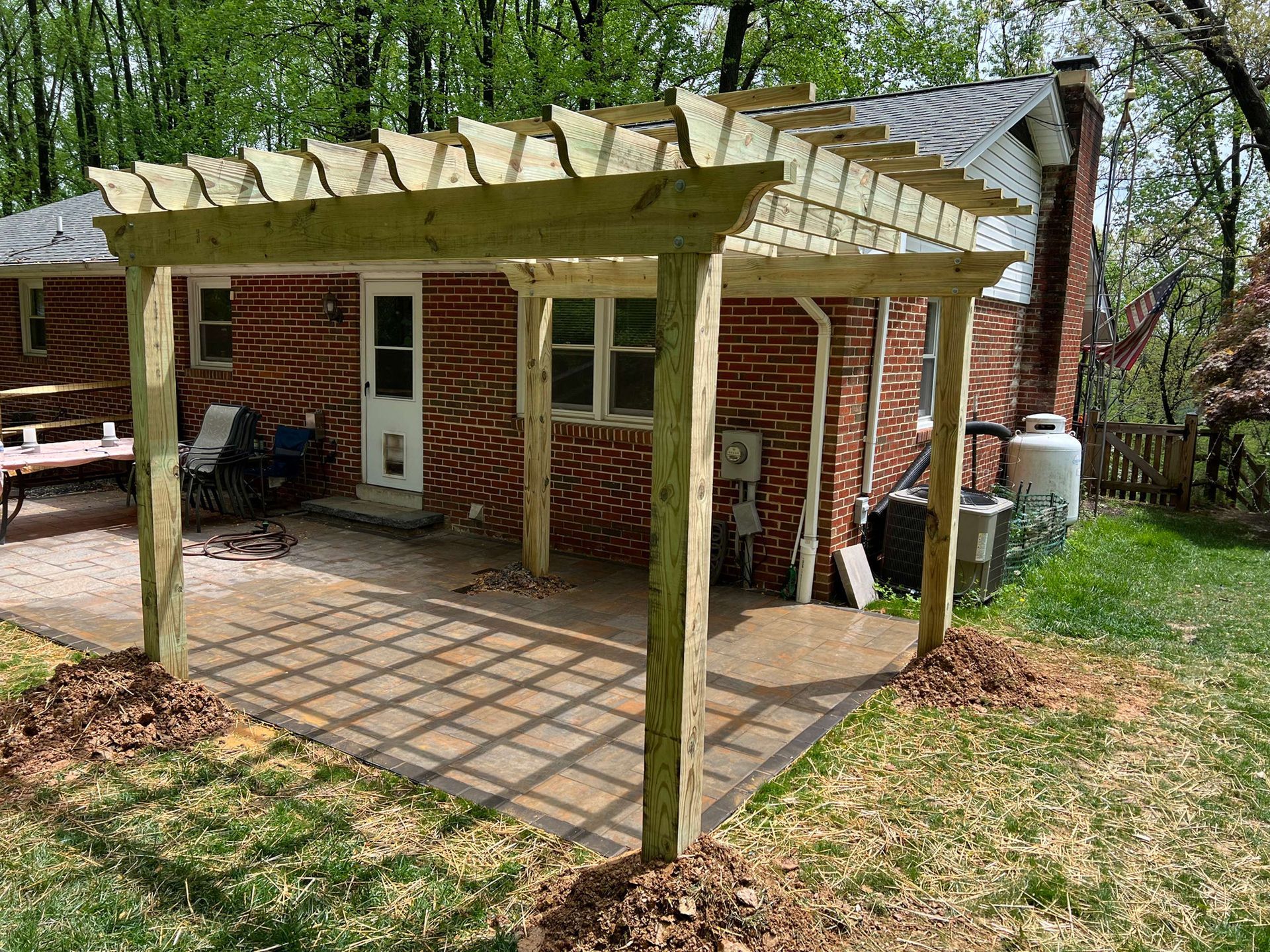A wooden pergola is sitting in the backyard of a brick house.