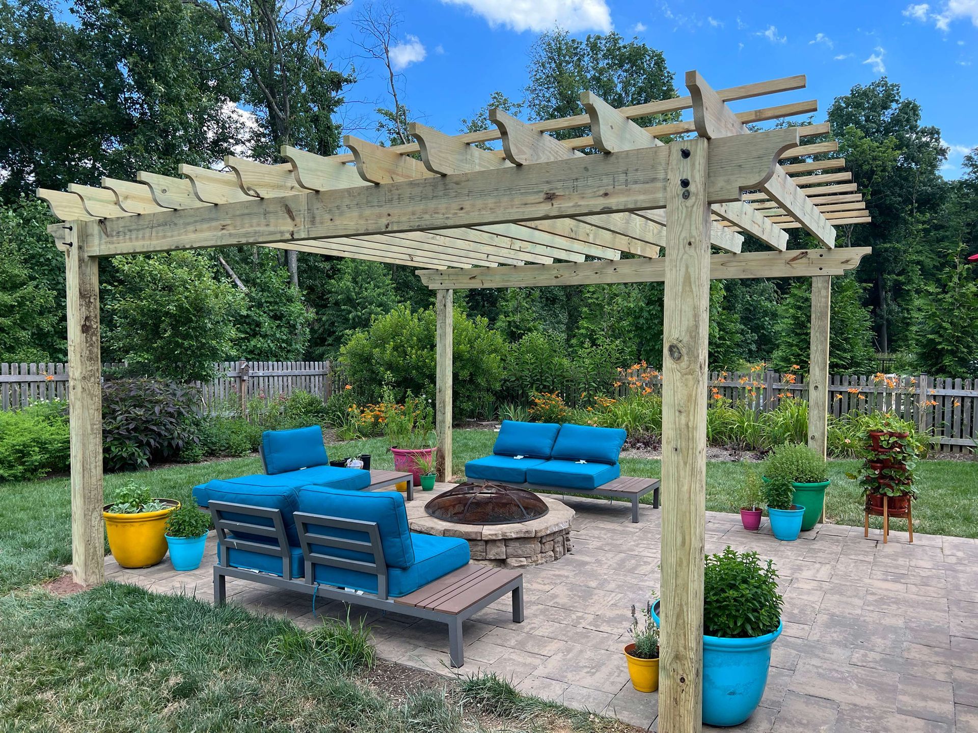 There is a fire pit under a pergola in the backyard.