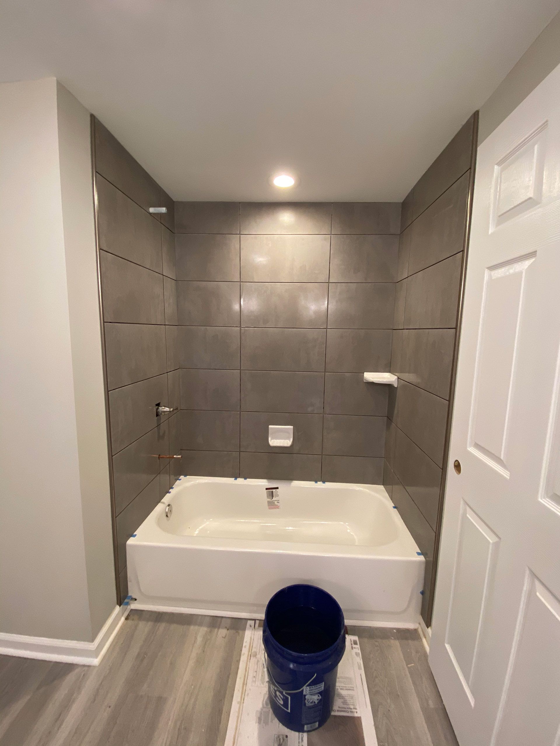 A bathroom with a bathtub and a blue bucket on the floor.