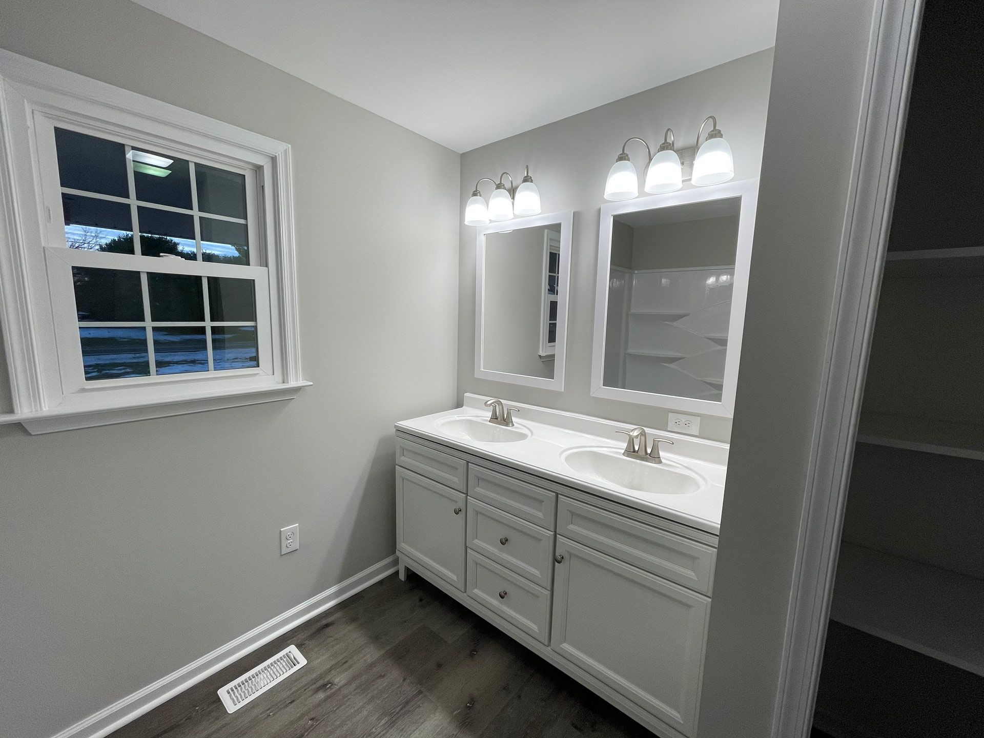 A bathroom with two sinks , two mirrors and a window.