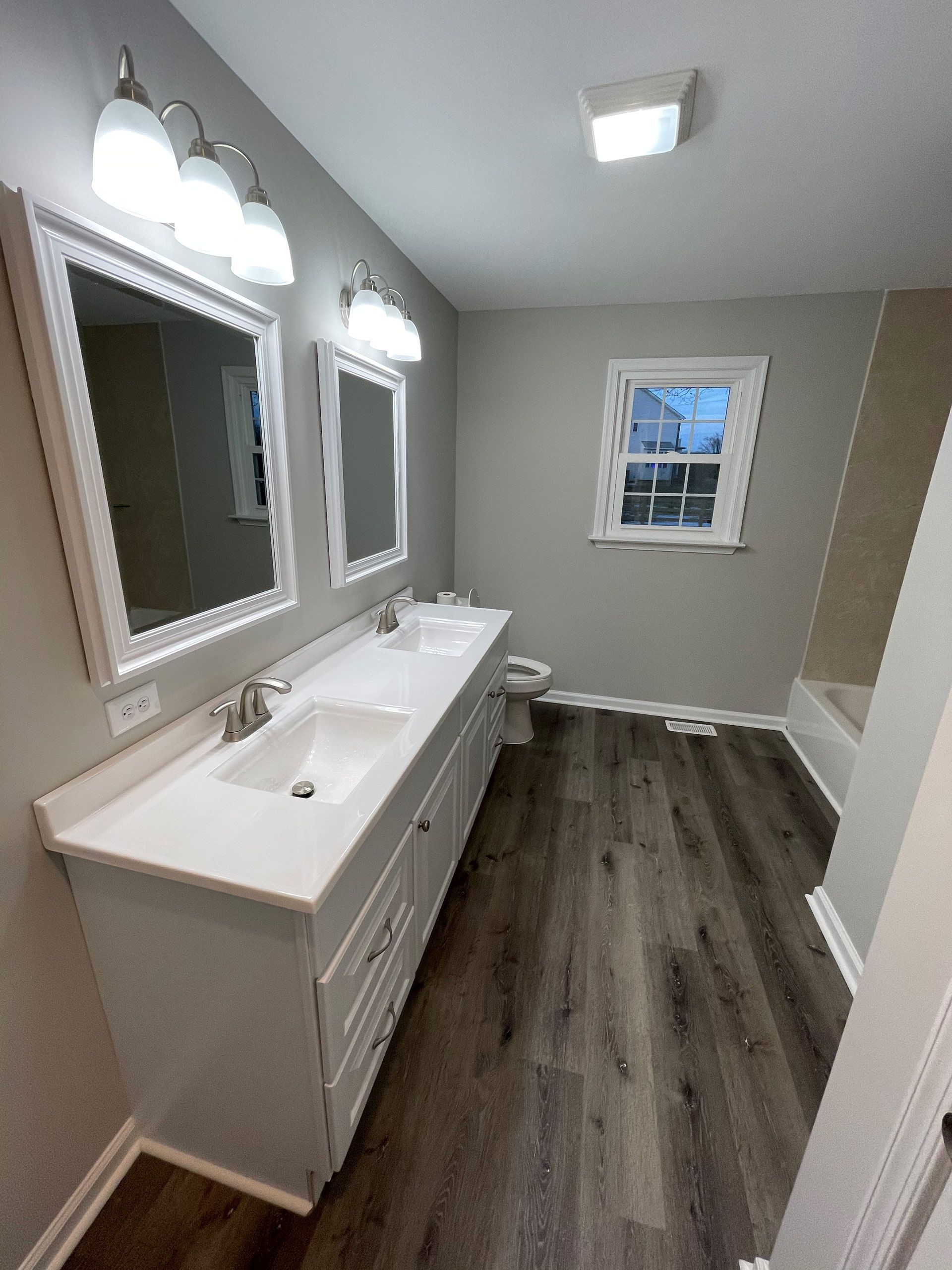 A bathroom with two sinks , a toilet , and a window.