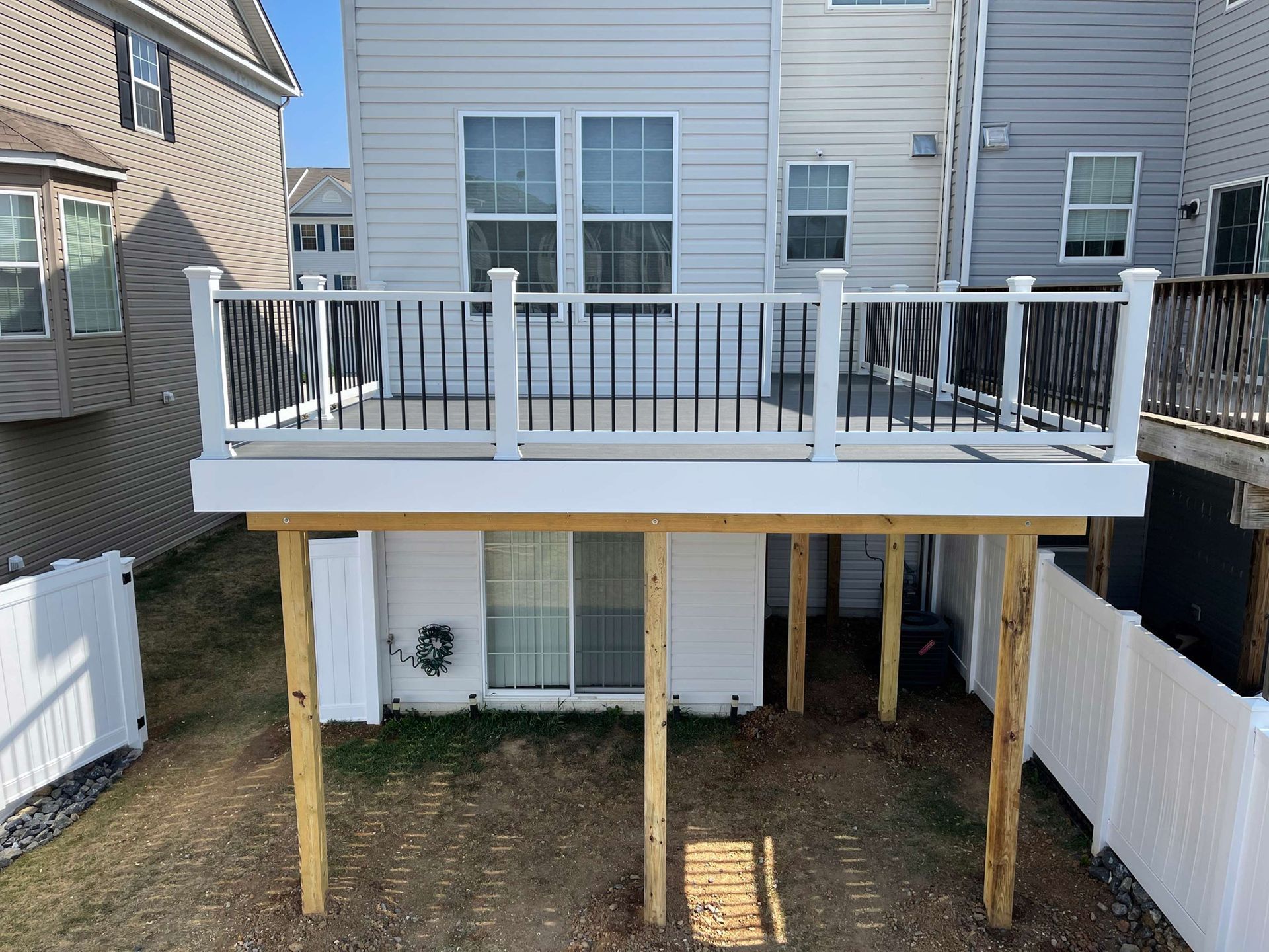 A white deck with a black railing is in the backyard of a house.