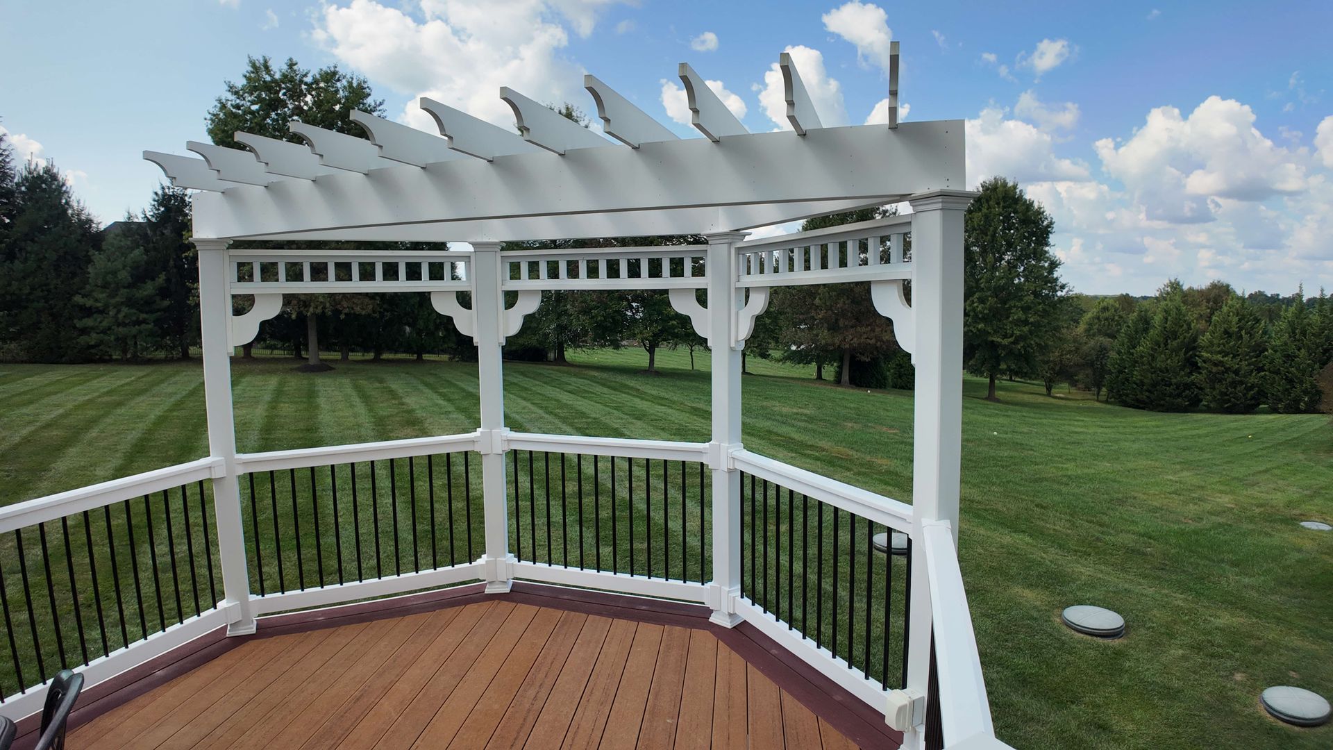 A deck with a pergola and a view of a lush green field.