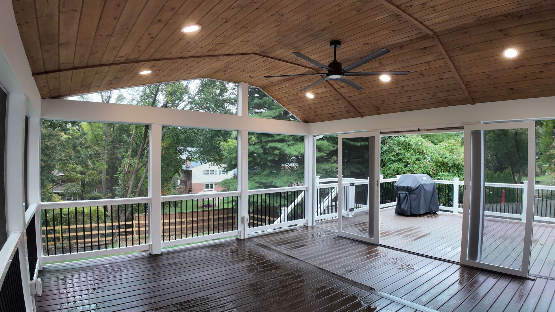 A screened in porch with a ceiling fan and a grill.
