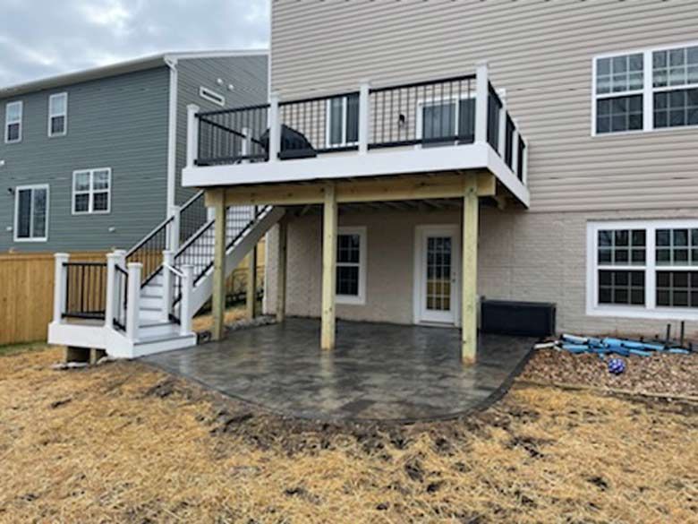 A large deck with stairs leading up to it is in the backyard of a house.