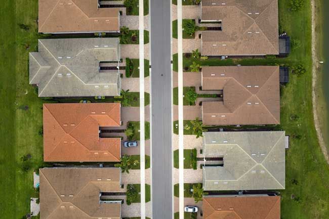 Aerial view of houses with different colored roofs along a straight road.