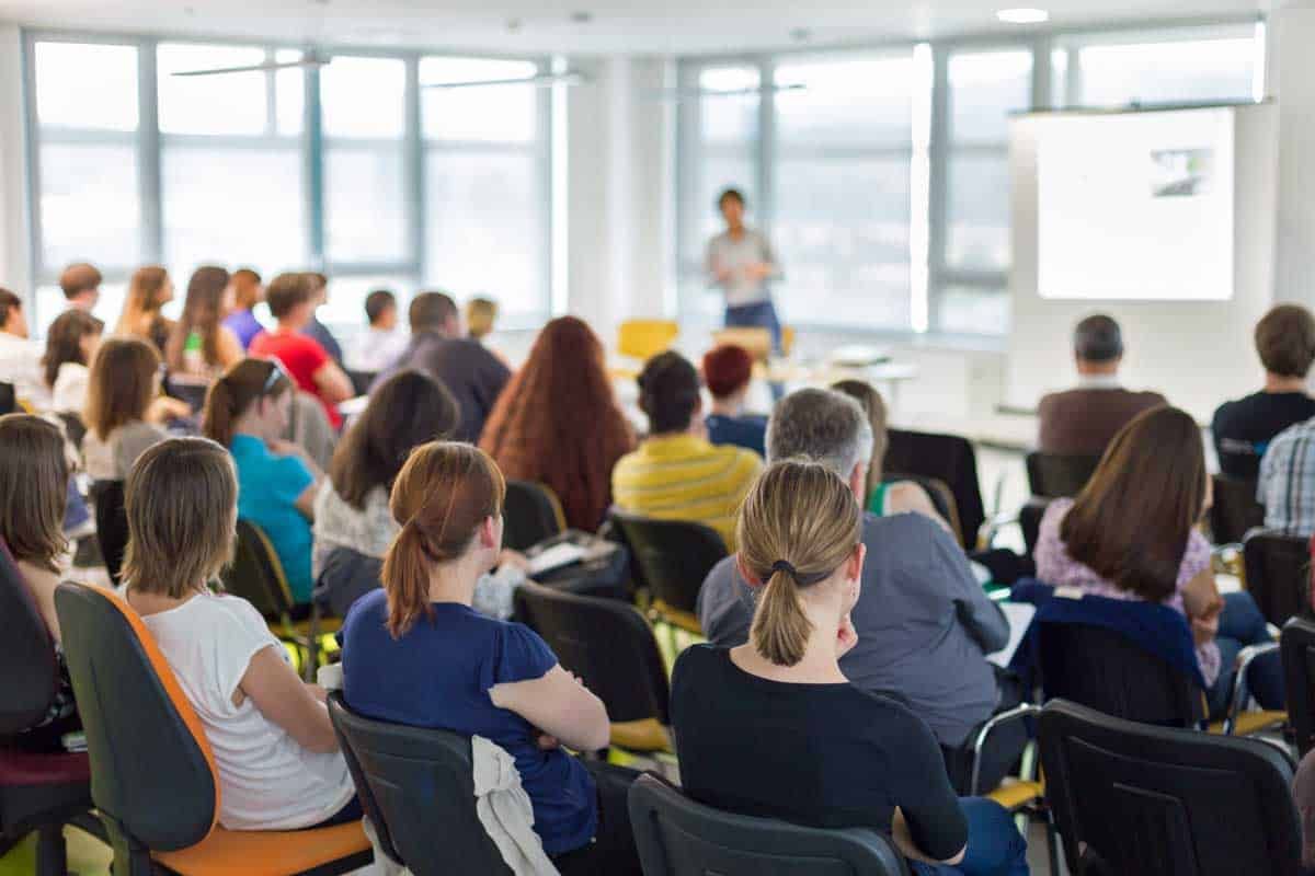 A group of people are sitting in a lecture hall watching a presentation.