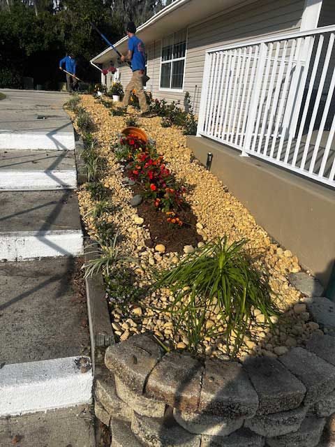 A man is standing next to a row of flowers in front of a house.
