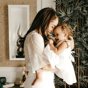 A woman in a white dress is holding a baby in her arms.