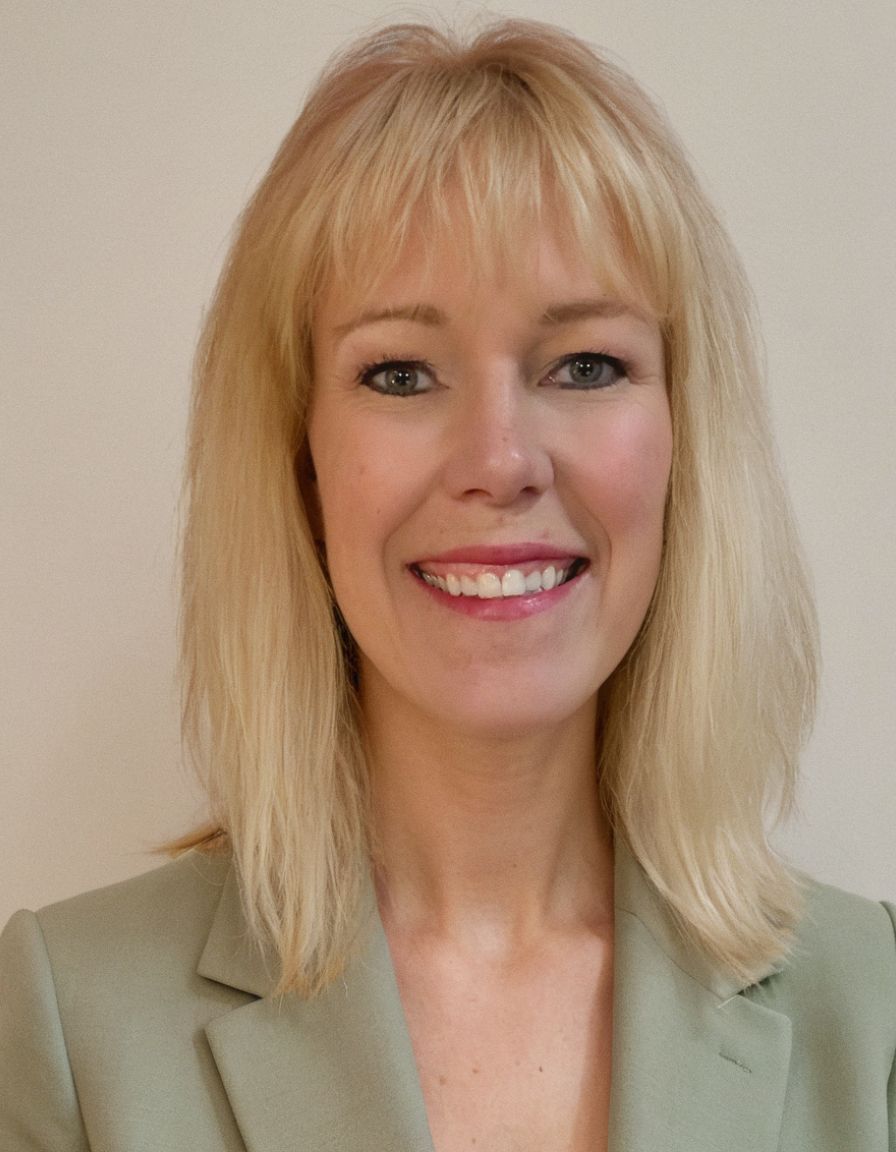 Woman with blonde hair smiling, wearing a light green blazer against a neutral background.