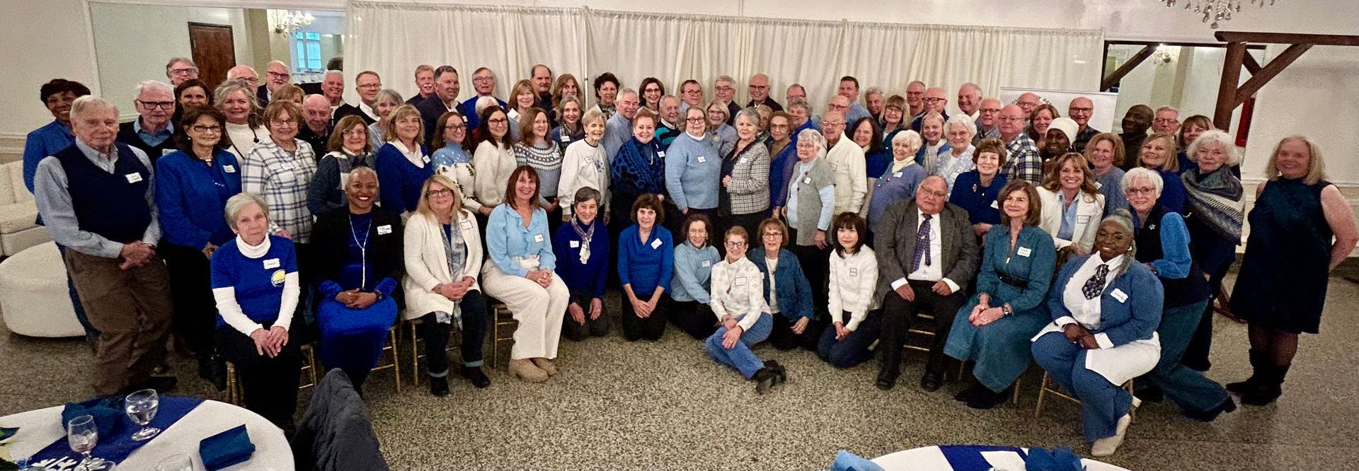 Group of people in blue shirts pose in front of a gazebo, park setting. Banner overhead.