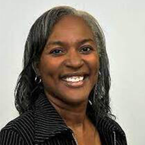Woman with gray hair smiling, wearing a black striped shirt against a white background.