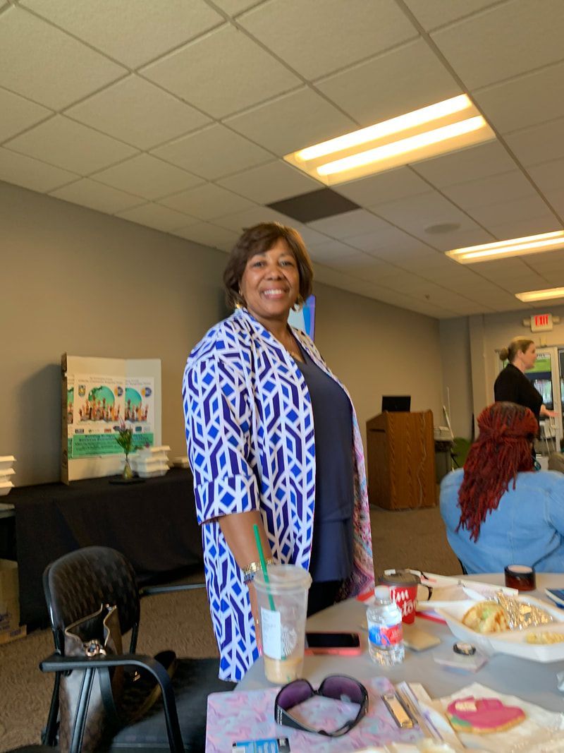 Woman smiles at the camera, wearing a blue and white patterned cardigan. Meeting room setting.