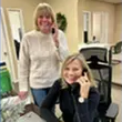 Two smiling women on the phone in an office; one standing, one sitting.