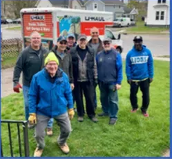 Men standing in front of a U-Haul truck on a lawn; some are wearing blue.