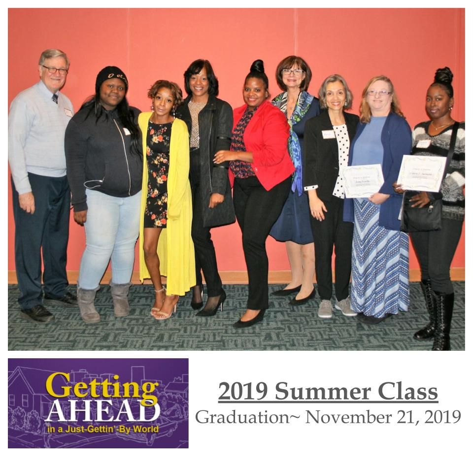 Group photo of the 2019 Summer Class graduation. Diverse group in formal attire, smiling in front of an orange wall.
