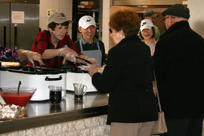 People being served food at a soup kitchen, with volunteers wearing hats.