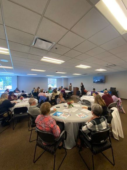 People seated at round tables in a conference room, listening to a presentation.