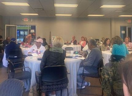 People seated at round tables in a brightly lit room; some are speaking.