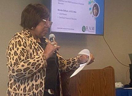 Woman in leopard print jacket speaks at a podium. A screen displays her name, title, and company logo.