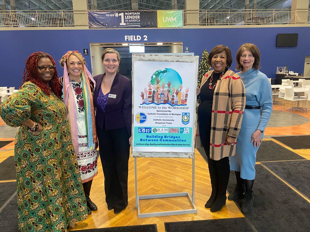 Five women pose with a poster for a cultural event, indoors, with a blue wall in the background.