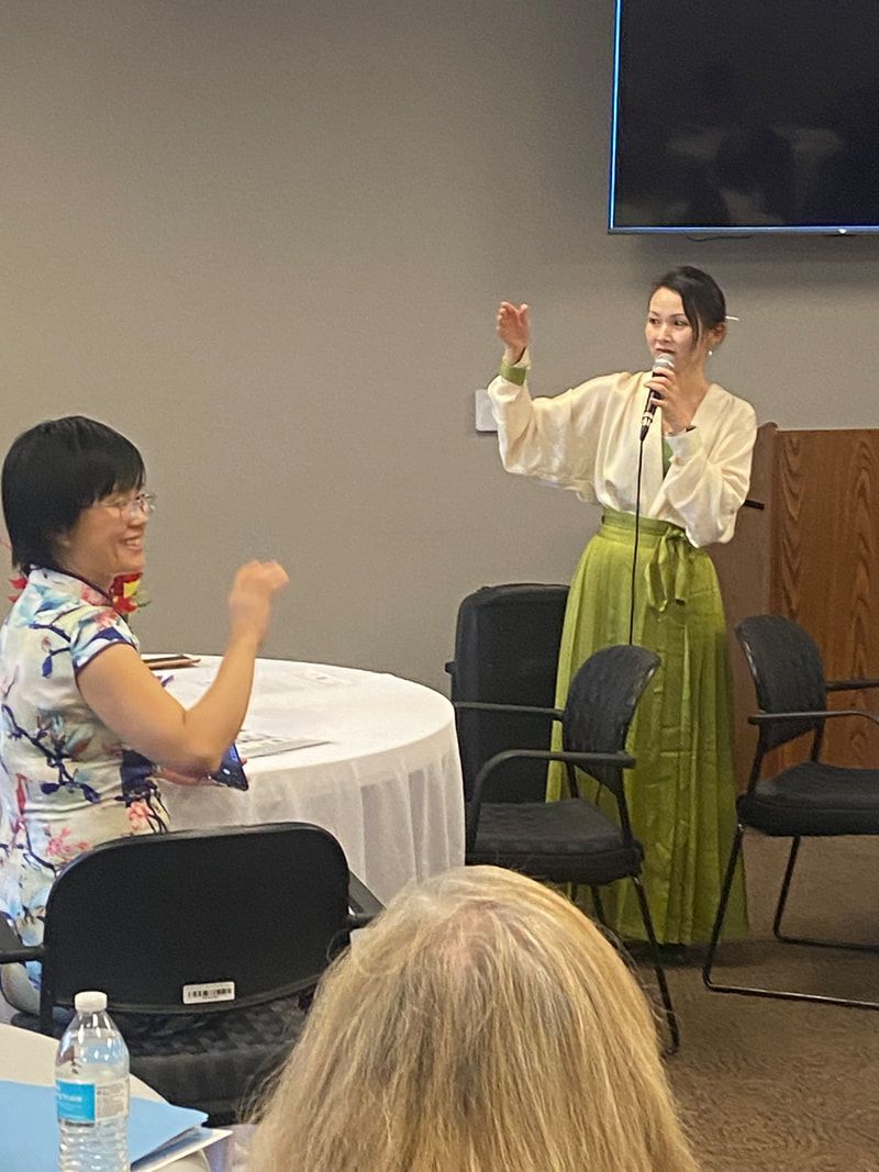 Woman in green skirt gestures, speaking to another woman at a table.