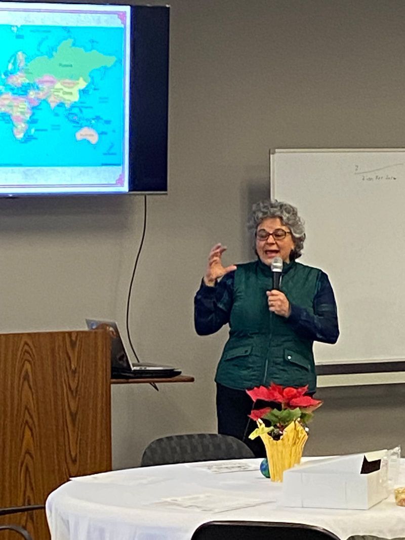 Woman giving presentation with world map on screen. She gestures, smiling.