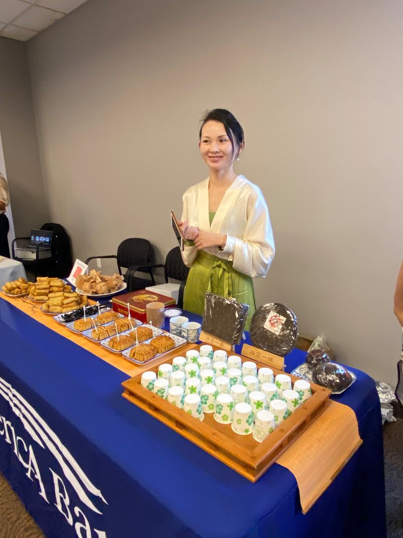 Woman at a table with food and drinks, smiling. Table has blue cloth, setting is indoors.