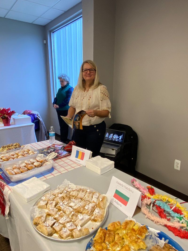 Woman at a table with pastries, flags, and a person in the background.
