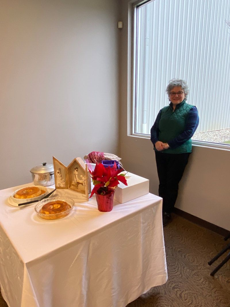 Woman in a green vest stands beside a table set with food and decorations near a window.