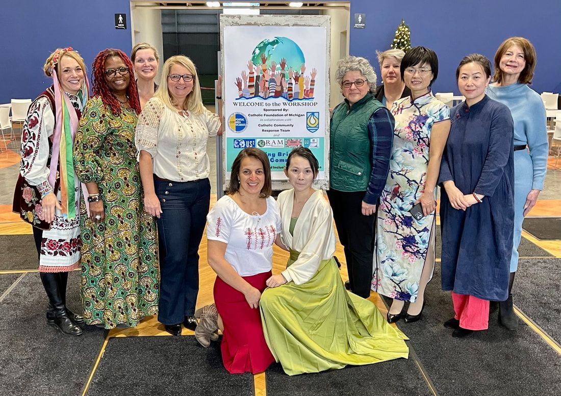 Group of women in cultural attire posing by a sign, some kneeling, smiling.
