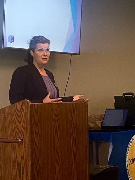 Woman giving a presentation from a podium with a screen behind her.