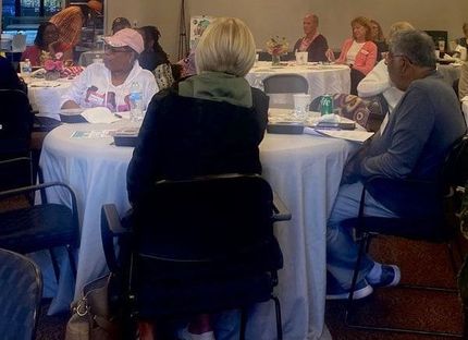 People seated at round tables in a well-lit room, likely attending a meeting or event.