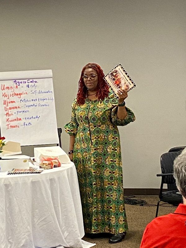 Woman in green dress presents at a table; whiteboard behind her with text.