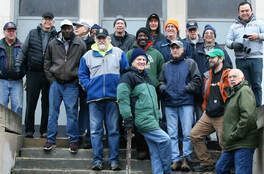 A group of diverse people stand on steps outdoors. They appear to be a work crew.