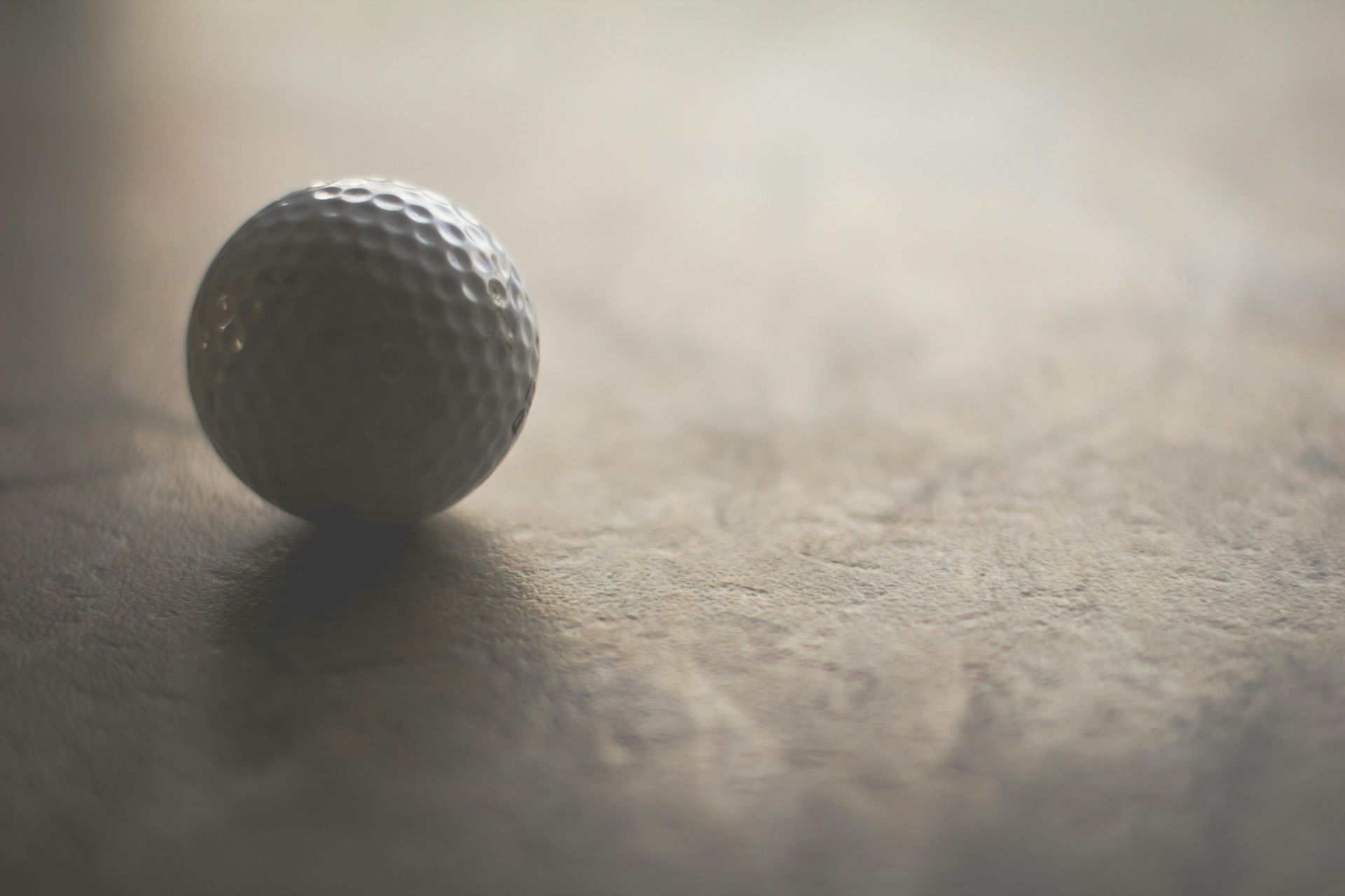 Golf ball resting on a textured, tan surface.