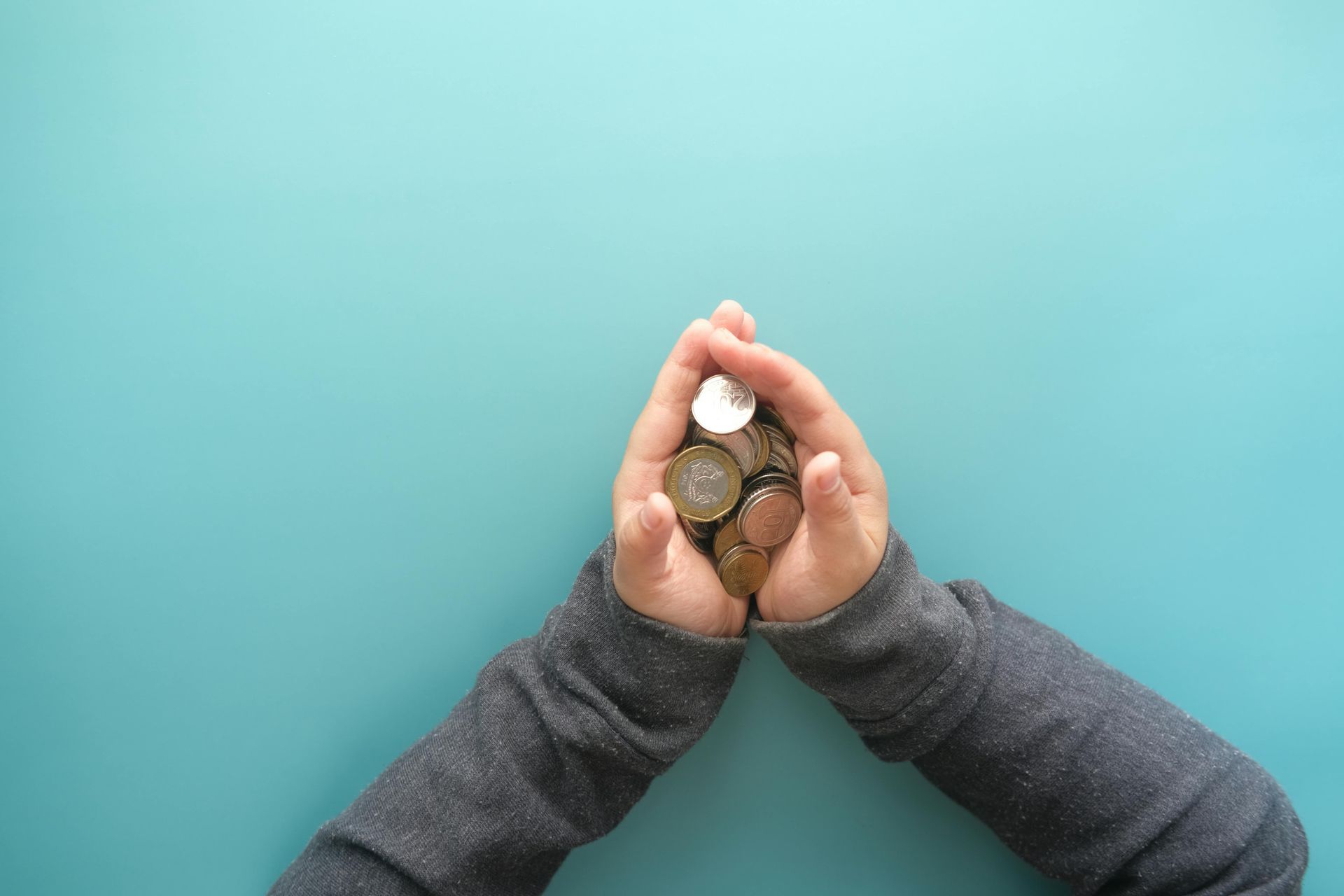 Hands holding a small pile of coins against a turquoise background.