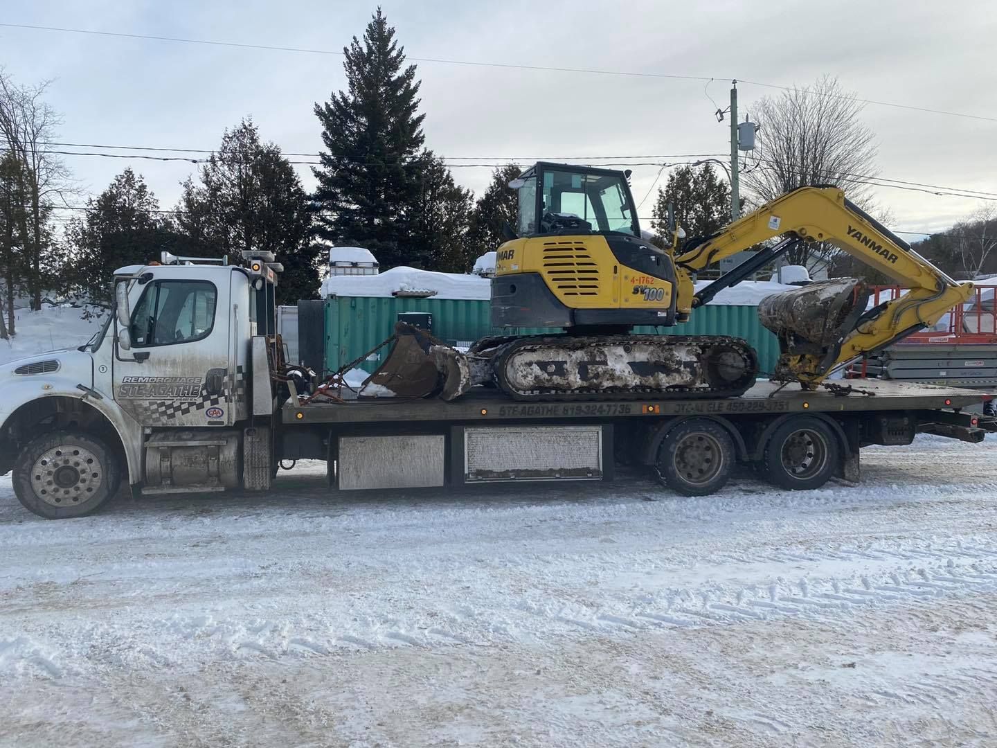 Une dépanneuse transporte une excavatrice jaune à l'arrière.
