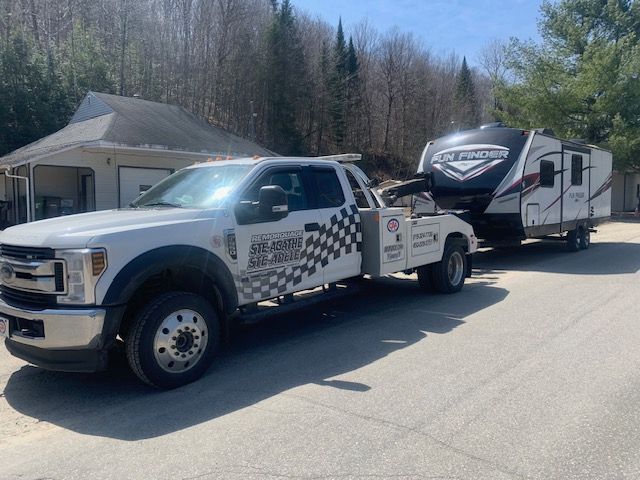 Une dépanneuse blanche remorque un camping-car sur une route.