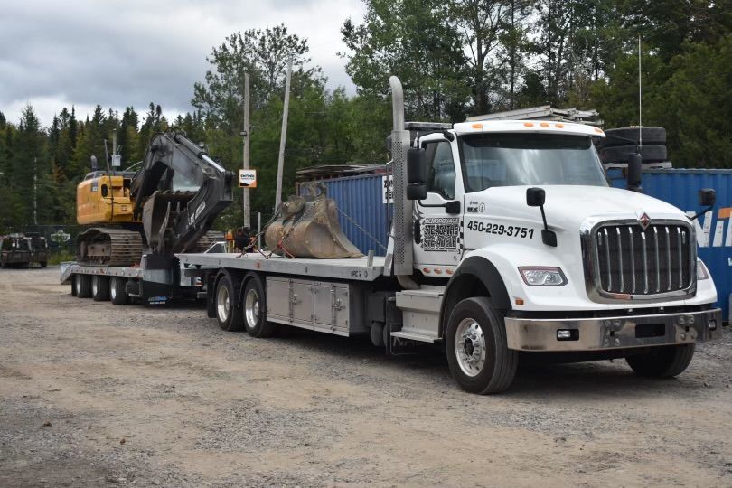 Un camion blanc transporte une excavatrice jaune sur une remorque à plateau.