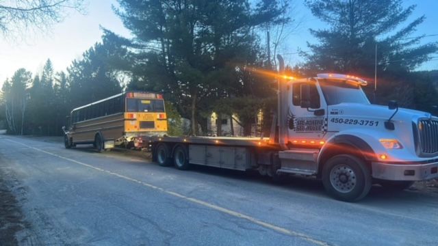 Une dépanneuse remorque un autobus scolaire sur une route.