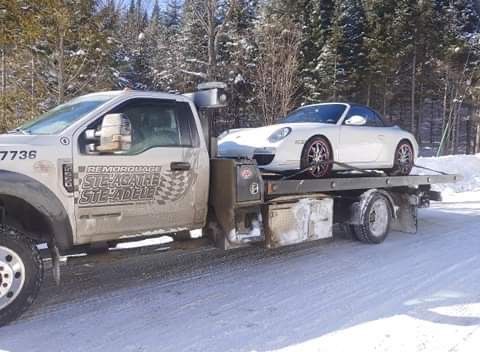 Une voiture blanche est remorquée par une dépanneuse dans la neige.