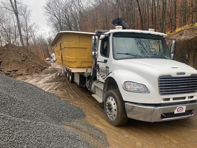 Un camion à benne basculante roule sur un chemin de terre à côté d'un tas de gravier.
