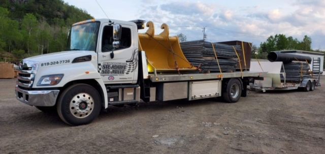 Un camion blanc avec un godet jaune à l'arrière est garé sur un terrain en terre.